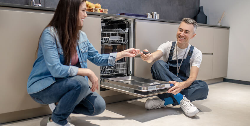 woman holding out tool to plumbing near dishwasher